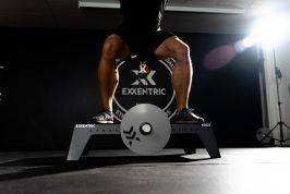 man squatting on kBox Pro with harness and L flywheel in a photo studio
