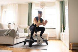 Sara squatting on kBox Active with harness and M flywheel in the living room