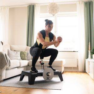 Sara squatting on kBox Active with harness and M flywheel in the living room