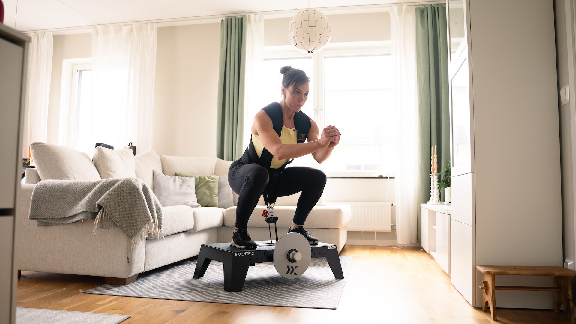 Sara squatting on kBox Active with harness and M flywheel in the living room